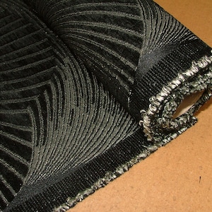 May include: A roll of black fabric with a silver metallic pattern. The fabric has a textured, woven look and a fringed edge.