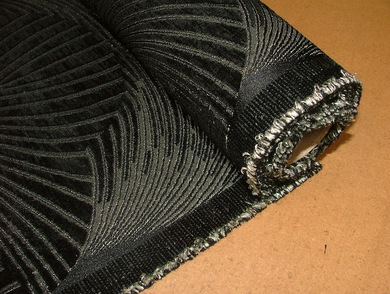 May include: A roll of black fabric with a silver metallic pattern. The fabric has a textured, woven look and a fringed edge.