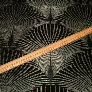 May include: Black fabric with a silver metallic geometric pattern. A wooden ruler is placed on top of the fabric, showing measurements in inches and centimeters.