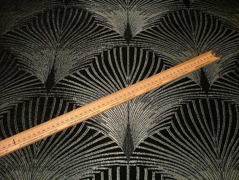 May include: Black fabric with a silver metallic geometric pattern. A wooden ruler is placed on top of the fabric, showing measurements in inches and centimeters.