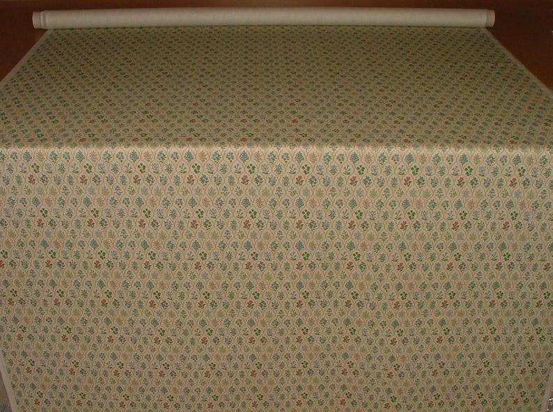 May include: A roll of fabric featuring a repeating pattern of small floral and leaf motifs in green, red, and blue on a cream background. The fabric is folded over a surface.