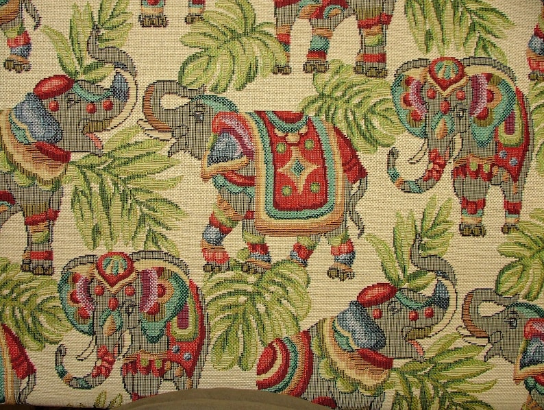 May include: A beige fabric with a repeating pattern of colorful elephants with intricate details. The elephants are adorned with red, blue, green, and yellow accents. The background is a cream color with green leafy patterns.
