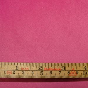 May include: A close-up of a bright pink fabric swatch with a wooden ruler measuring 4 inches. The ruler is labeled "1 inch" and has markings in centimeters.