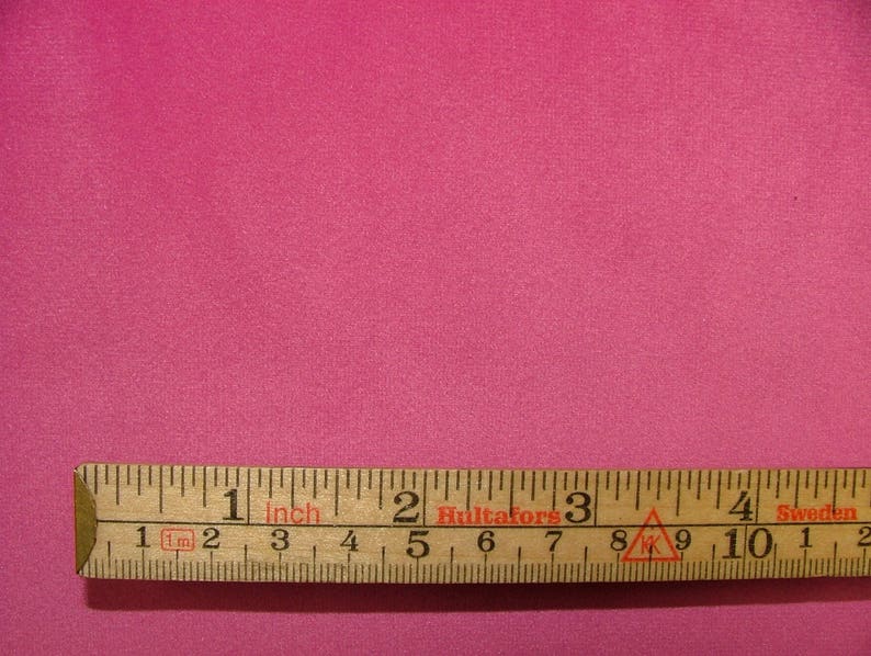 May include: A close-up of a bright pink fabric swatch with a wooden ruler measuring 4 inches. The ruler is labeled "1 inch" and has markings in centimeters.
