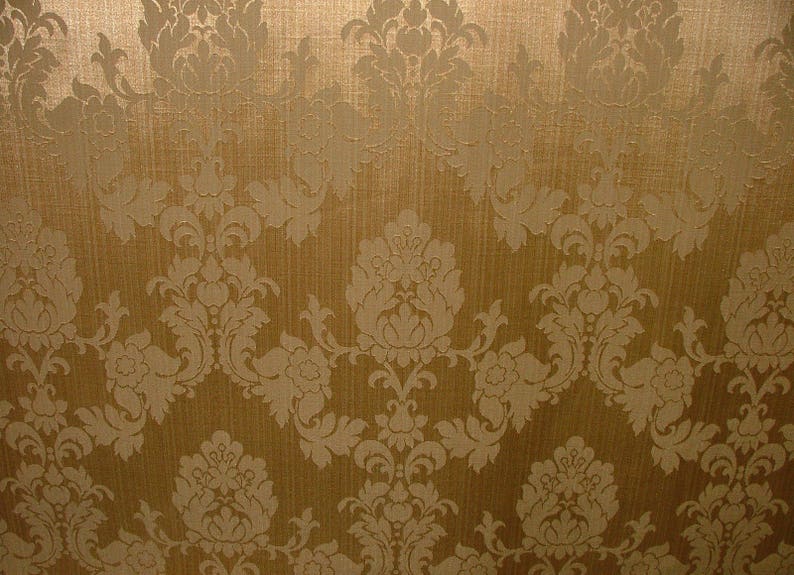 K&ouml;nnte beinhalten: Ein goldener Hintergrund mit einem wei&szlig;en Damastmuster. Das Muster ist ein sich wiederholendes Design aus stilisierten Blumen und Bl&auml;ttern.