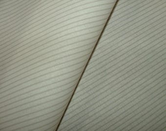 May include: Close-up of a folded fabric with a subtle striped pattern. The fabric is a light beige color with thin, parallel stripes in a slightly darker shade. The texture appears soft and possibly woven.