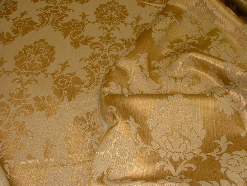 K&ouml;nnte beinhalten: Nahaufnahme eines goldenen Stoffes mit Damastmuster. Der Stoff hat einen dezenten Glanz und ein erhabenes Design.