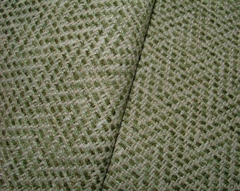 May include: Close-up of a textured fabric with a woven pattern. The fabric is primarily a light green color with a subtle, interwoven design. The texture appears slightly rough, with a mix of light and dark green threads.