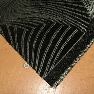 May include: Close-up of a black fabric with a silver geometric pattern. The fabric has a raw edge and is folded over on itself.