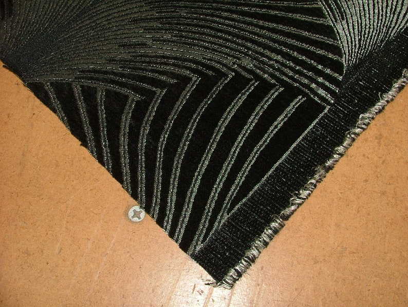 May include: Close-up of a black fabric with a silver geometric pattern. The fabric has a raw edge and is folded over on itself.