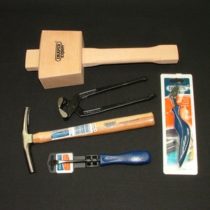 May include: A collection of carpentry tools, including a wooden mallet, nail pullers, a tack hammer, and a staple remover. The tools are displayed on a black surface. The mallet has "Draper Expert" printed on it.