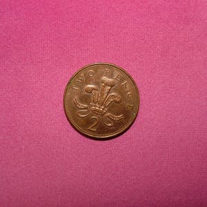 May include: A copper-colored British two pence coin with the inscription "TWO PENCE" and a royal crest featuring a crown and three feathers.