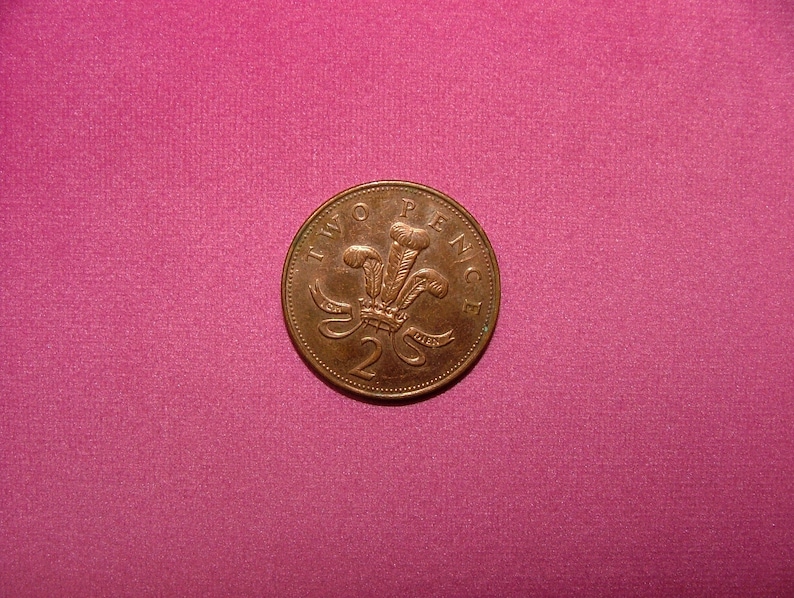 May include: A copper-colored British two pence coin with the inscription "TWO PENCE" and a royal crest featuring a crown and three feathers.