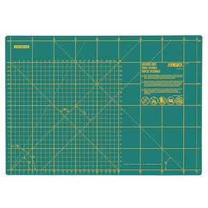 May include: Green self-healing cutting mat with a grid pattern in yellow. The mat is labeled "Folding Mat, Tapet Pliabla, Tepete Plegable" and has a warning symbol with text in Spanish and English. The mat is 45 cm by 30 cm.