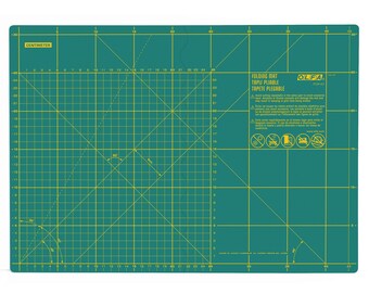 Könnte beinhalten: Grüne, selbstheilende Schneidematte mit einem gelben Gittermuster. Die Matte ist mit "Folding Mat, Tapet Pliabla, Tepete Plegable" beschriftet und hat ein Warnsymbol mit Text in Spanisch und Englisch. Die Matte ist 45 cm x 30 cm groß.