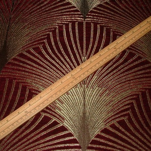 May include: Red fabric with a gold and brown geometric pattern. The fabric has a subtle sheen and a textured surface.