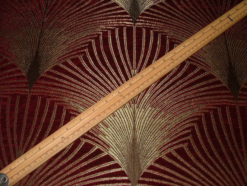 May include: Red fabric with a gold and brown geometric pattern. The fabric has a subtle sheen and a textured surface.