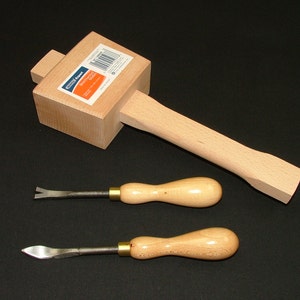 Puede incluir: Un mazo de madera con una cabeza rectangular y un mango largo, junto con dos cinceles de metal con mango de madera. El mazo tiene una etiqueta que dice "Project Expert".