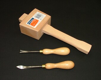 May include: A wooden mallet with a rectangular head and a long handle, alongside two wood carving chisels. The chisels have metal blades and wooden handles. The tools are light brown and sit on a black surface.