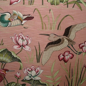 May include: A pink fabric with a repeating pattern of green leaves, pink and white flowers, and birds. The birds are a brown heron with its wings spread and a green and brown duck.