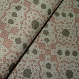 May include: Close-up of folded fabric with a repeating pattern in pink, grey, and white. The design features geometric shapes and circular elements, creating a textured appearance. The fabric appears to be a woven material, suitable for various textile projects.