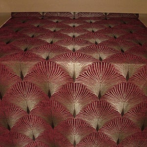 May include: Red fabric with a gold geometric pattern of overlapping fans. The fabric has a subtle sheen and a textured surface.