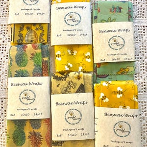May include: Several packages of beeswax wraps are displayed, each containing three wraps in various sizes. The wraps feature colorful patterns including bees, pineapples, and floral designs. Each package is labeled with the text "Beeswax Wraps".