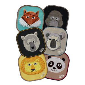 Op de afbeelding: Zes geborduurde patches met verschillende dieren, waaronder een vos, een gorilla, een ijsbeer, een koala, een leeuw en een panda. Elke patch heeft een blauw en geel "SOS" geborduurd.