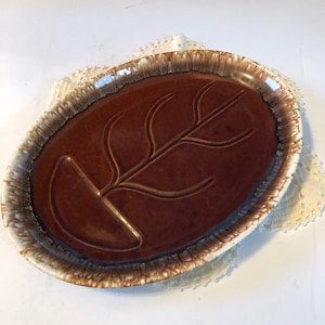 May include: A brown and white oval ceramic serving dish with a leaf design. The dish has a brown glaze with a white rim and a white glaze on the bottom.