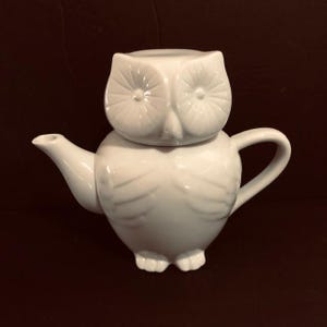 May include: White ceramic teapot shaped like an owl with a lid that is also shaped like an owl. The teapot has a spout and a handle.