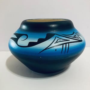 May include: A hand-painted ceramic pot with a rounded shape and a wide opening. The pot features a gradient of blue hues, with black and white geometric designs. The interior is a light beige color.