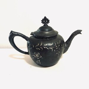May include: A black silver plated teapot with a floral design. The teapot has a decorative handle and spout.