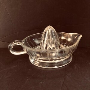 May include: A clear glass citrus juicer with a ribbed bowl and a pointed reamer. The juicer has a handle on the side.