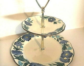 May include: Two-tiered serving stand with a gold metal handle. The stand is decorated with a blue and green floral pattern.