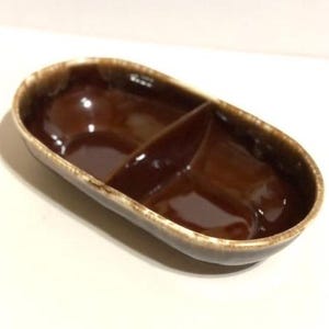 May include: A brown ceramic divided serving dish. The oval-shaped dish has two compartments and a glossy finish. The rim has a lighter brown color. This dish is suitable for serving snacks or condiments.