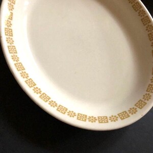 May include: A white ceramic plate with a gold border featuring a repeating pattern of small flowers and squares.