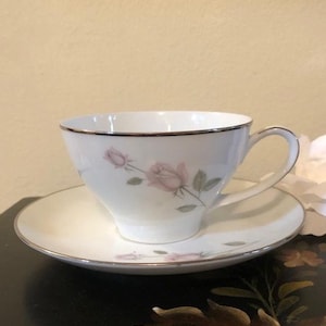 May include: A white teacup and saucer set with a delicate pink rose design and a silver rim.