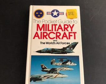 May include: A white paperback book titled The Pocket Guide to Military Aircraft and The World's Air Forces, edited by David Donald. The cover features a yellow price sticker, a blue and yellow emblem, a star logo, and images of fighter jets.