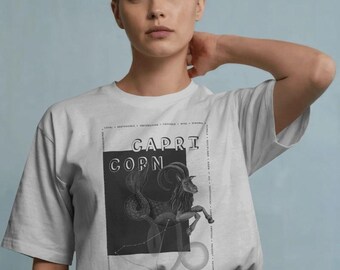 Puede incluir: Una camiseta blanca de manga corta con un estampado gráfico negro de un Capricornio. El diseño incluye el texto CAPRICORN, un diagrama de constelación y un borde con palabras descriptivas como LOYAL, RESPONSIBLE y AMBITIOUS.