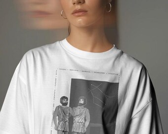 Puede incluir: Una camiseta blanca con un estampado gráfico en blanco y negro del signo zodiacal Géminis. El diseño incluye dos figuras con vestimenta clásica, un mapa de constelaciones y una lista vertical de palabras descriptivas como curioso e ingenioso.