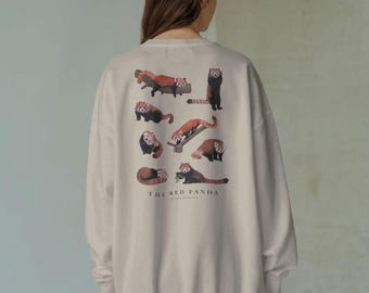Puede incluir: Sudadera beige con ilustraciones de pandas rojos en varias poses. El texto "THE RED PANDA" está impreso debajo. La sudadera tiene cuello redondo y mangas largas.