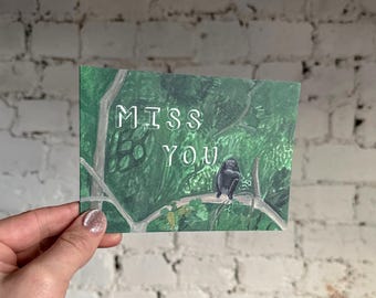 Puede incluir: Una tarjeta de felicitación con las palabras "MISS YOU" en letras blancas. La tarjeta presenta una ilustración en acuarela de un mono posado en una rama de árbol en un exuberante entorno forestal verde.