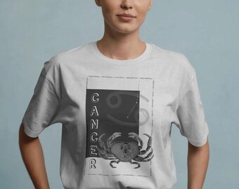 Puede incluir: Una camiseta gris claro de manga corta con un gráfico rectangular en el pecho. El diseño incluye la palabra CANCER en vertical, una ilustración de un cangrejo, el símbolo del zodiaco Cáncer y texto pequeño con rasgos de personalidad.