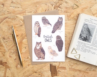 May include: A greeting card featuring watercolor illustrations of various British owl species, including short-eared, little, and long-eared owls. The card is on a wooden surface with a pen and a book with a bookmark.