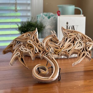 May include: A dragon sculpture made from rolled pages of a book. The dragon is brown and white and has its wings spread out. The dragon's tail is curled up in a spiral.