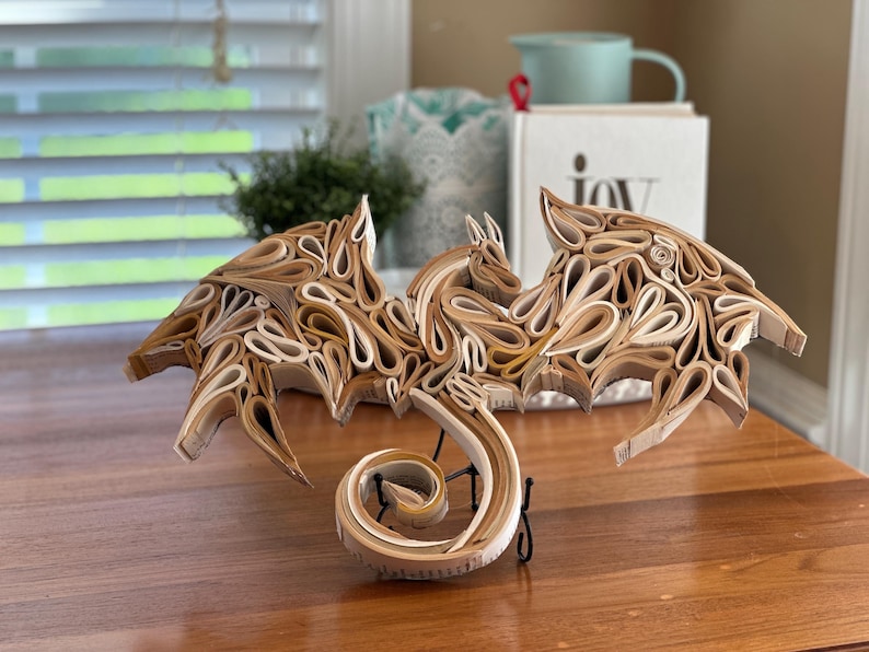 May include: A dragon sculpture made from rolled pages of a book. The dragon is brown and white and has its wings spread out. The dragon's tail is curled up in a spiral.
