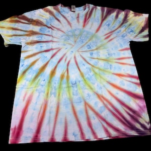 Op de afbeelding: Een tie-dye t-shirt met een spiraalpatroon. Het shirt heeft een mix van kleuren, waaronder blauw, geel, oranje, rood en paars. Het ontwerp straalt uit het midden van het shirt.