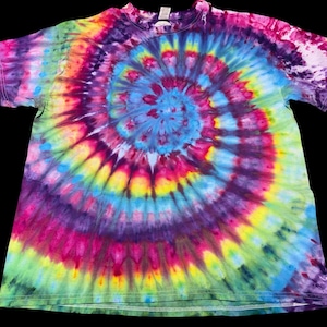 Op de afbeelding: Een kleurrijk tie-dye t-shirt met een spiraalvormig ontwerp. Het shirt heeft een levendige mix van kleuren, waaronder blauw, paars, roze, geel en groen. Het ontwerp is gecentreerd op het shirt en straalt naar buiten. Het t-shirt is gemaakt van een zacht materiaal.