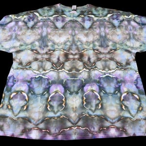 May include: A tie-dye t-shirt in shades of blue, purple, and gray. The shirt features a symmetrical pattern with wavy lines and organic shapes. The fabric appears soft and comfortable, with a crew neck and short sleeves.