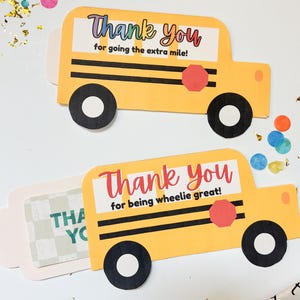 May include: Two yellow school bus-shaped cards with black wheels and a red stop sign. One card reads "Thank You for going the extra mile!" and the other says "Thank You for being wheelie great!" Confetti and a measuring tape are scattered around.